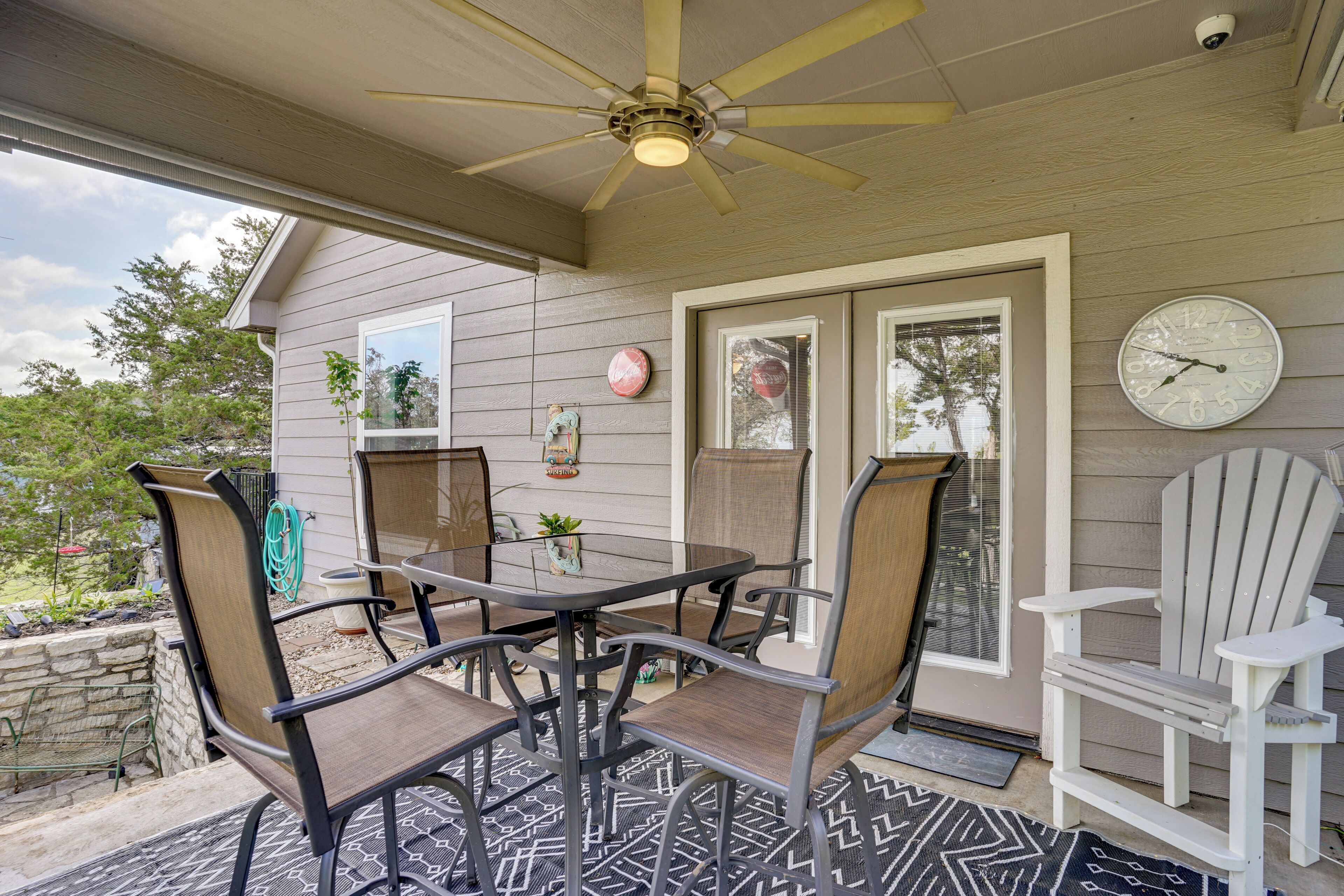 A covered patio with a table and chairs, a ceiling fan, a clock, and a door with a window.