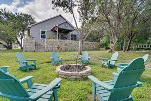 A house with a stone exterior, a porch with outdoor seating, and a fire pit surrounded by Adirondack chairs. - Walk to Lake Granbury: Home w/ Fire Pit! (Granbury)