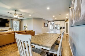 A modern living room with a wooden dining table, white chairs, a brown sofa, and a ceiling fan. - Walk to Lake Granbury: Home w/ Fire Pit! (Granbury)