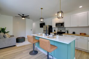 Eine moderne Küche mit einer zentralen Kochinsel, Barhocker, einem Deckenventilator und weißen Küchenschränken.