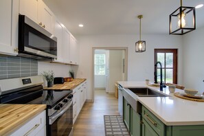 Moderni keittiö, jossa on mikroaaltouuni, liesi ja puinen työtaso.