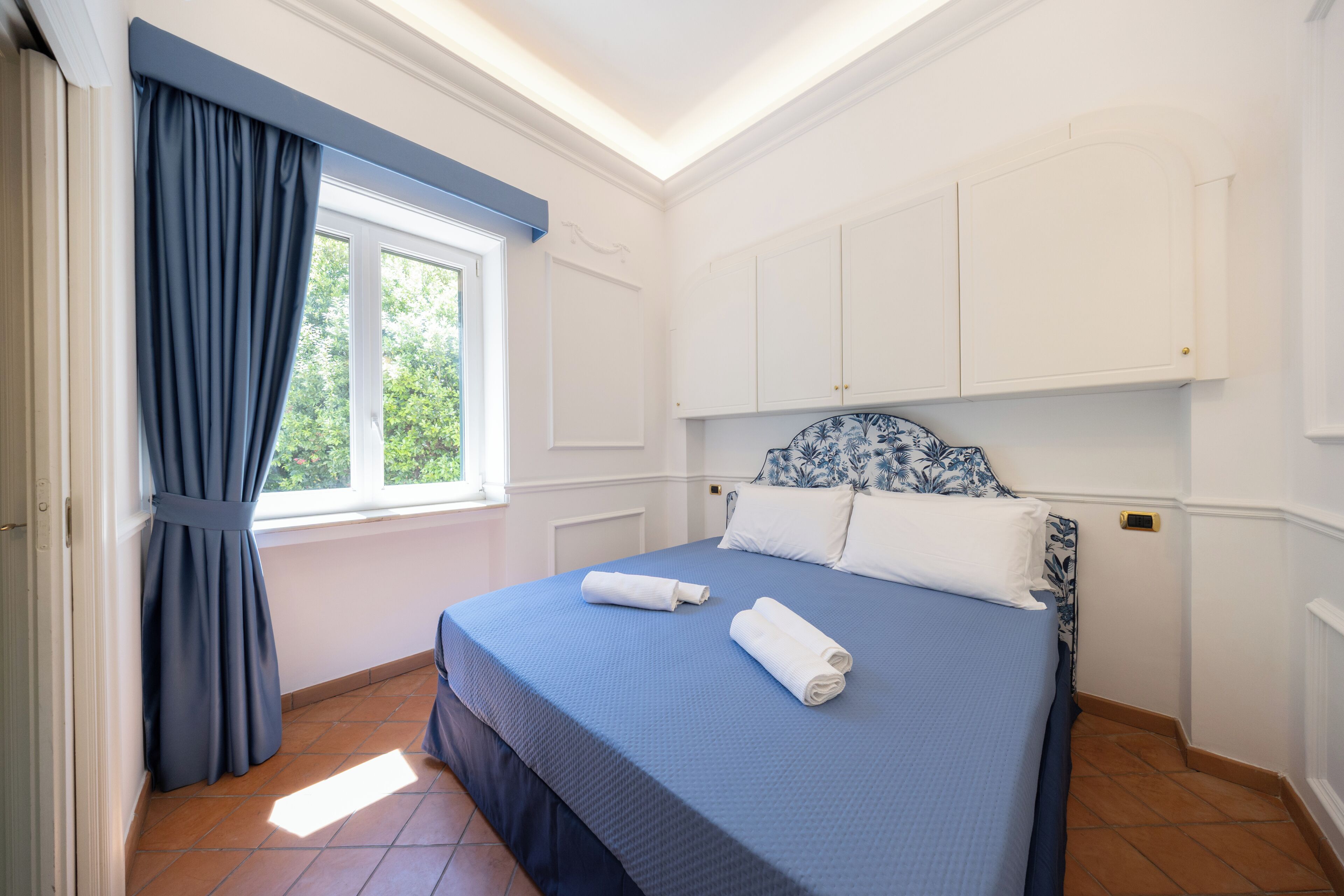 Un dormitorio con cama, cortinas, una ventana y muebles blancos.