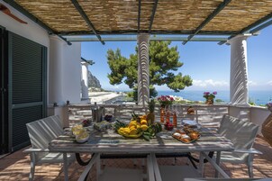 Un tavolo apparecchiato con frutta, dolci e bevande su una terrazza con vista sul mare.