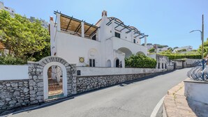 Una calle con un edificio blanco, paredes de piedra, arcos y techo de tejas.