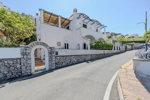 Una strada con un edificio bianco, caratterizzato da muri in pietra, portali ad arco e un tetto in tegole.