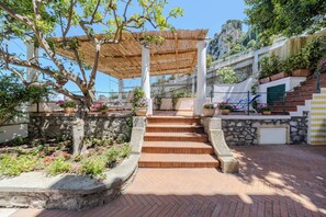 A stone staircase leading to a covered area with a pergola, surrounded by potted plants and a view of a mountainous landscape. - Villa Preziosa - Panoramic Sea View (Capri)