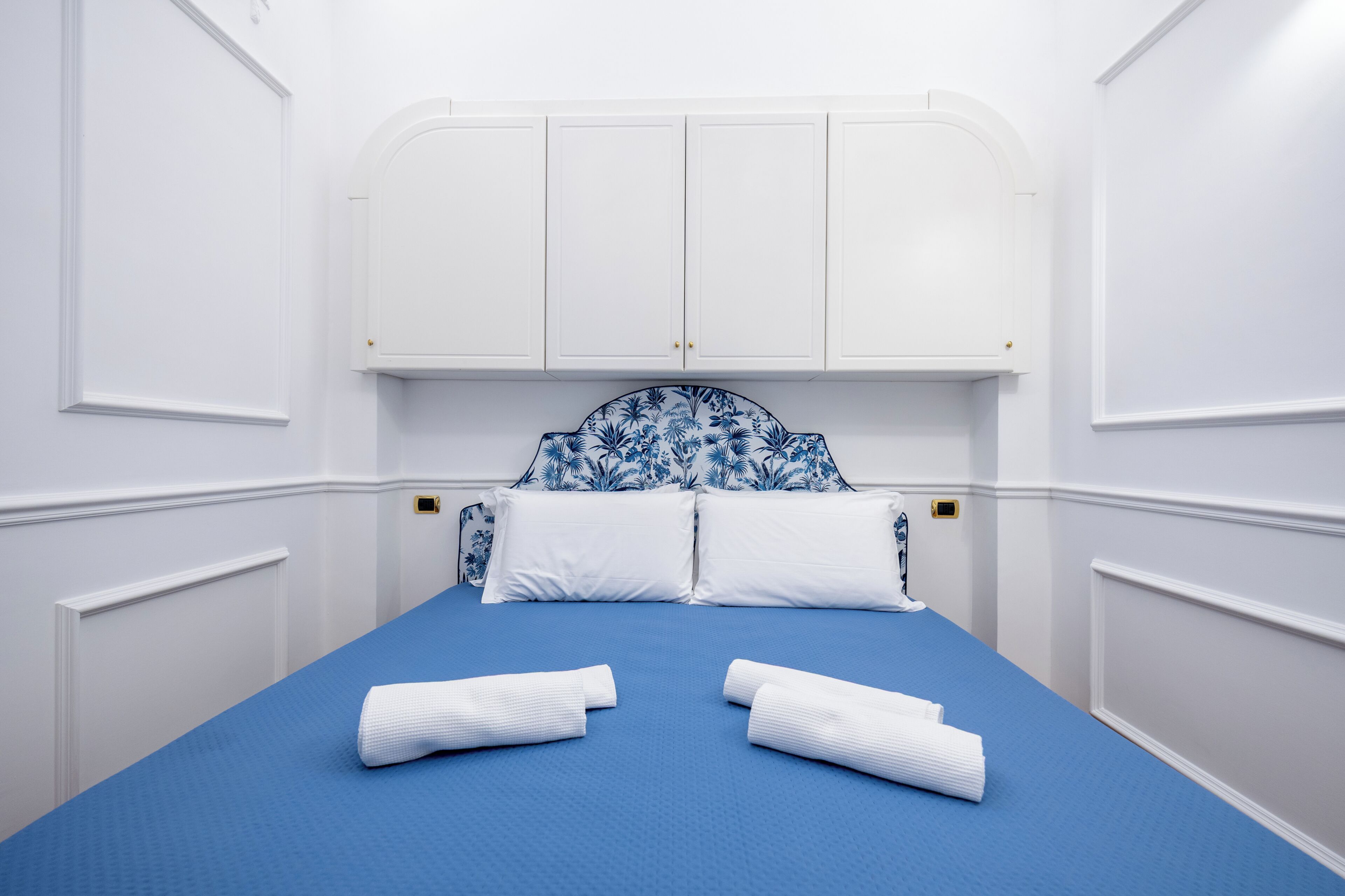 Ein Zimmer mit einem Bett, weißen Wänden und einem blauen Kopfteil.