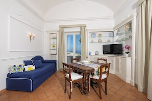 Un soggiorno con un divano blu, un tavolo da pranzo in legno, sedie, una TV e mensole con oggetti decorativi.