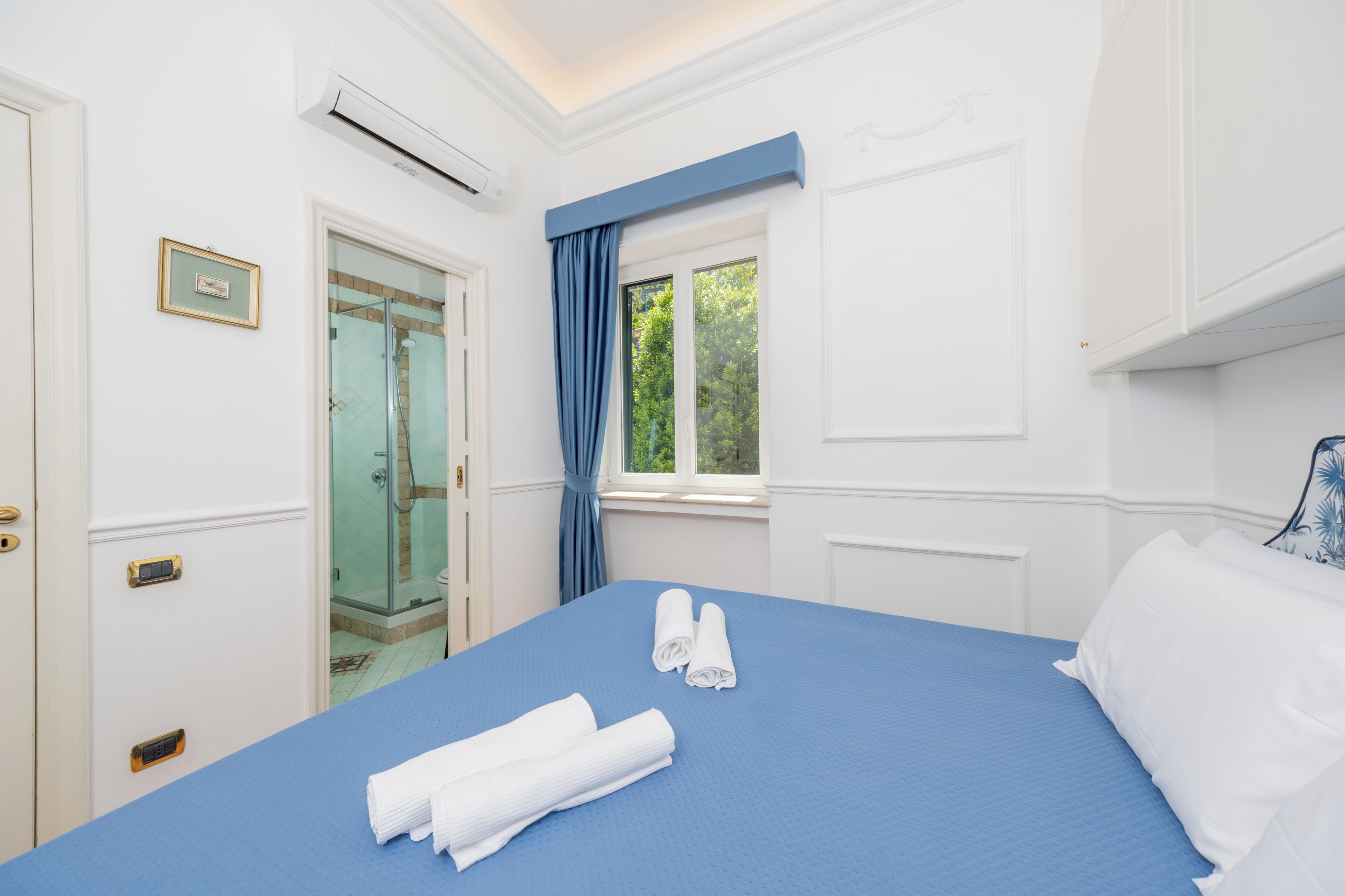 Una habitación de hotel con una cama, un baño con ducha de vidrio y una ventana con cortinas.