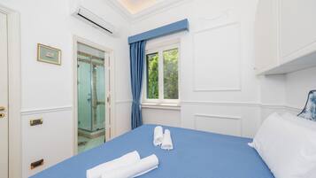 Una habitación de hotel con una cama, un baño con ducha de vidrio y una ventana con cortinas.