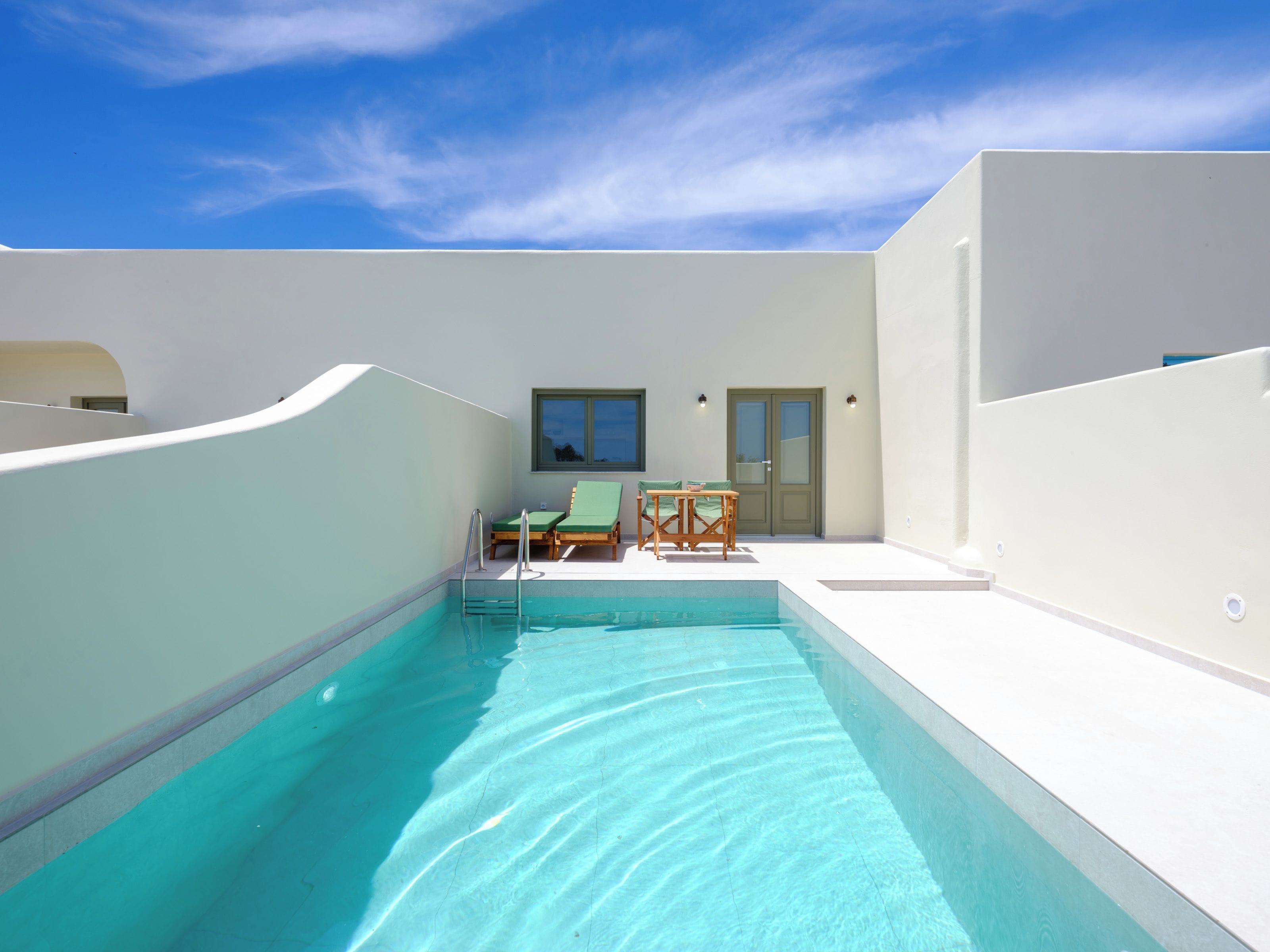 A swimming pool with a sun terrace, lounge chairs, and a table.