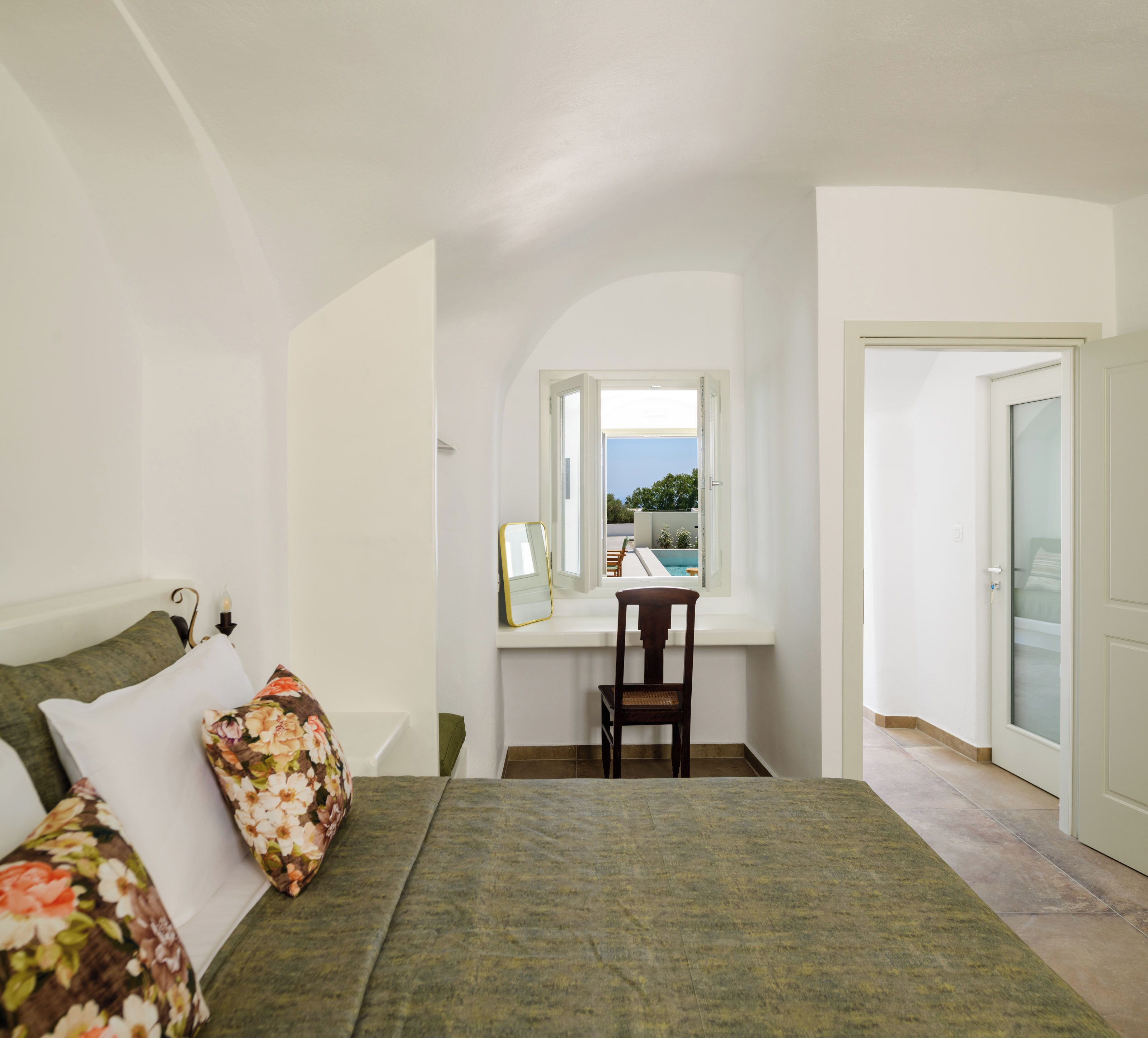 A bedroom with a bed, a desk, and a view of the outdoors.