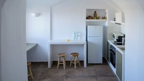 A kitchen with a white countertop, two stools, a refrigerator, and a microwave. - A Cycladic home with a private pool and sea view, away from the crowds! (Exo Gonia)