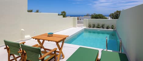 Área de piscina no terraço com mesa e cadeiras, uma mesinha com uma tigela e espreguiçadeiras.