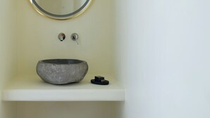 A bathroom with a round mirror, a stone sink, a wooden stool, and a white shelf. - A Cycladic home with a private pool and sea view, away from the crowds! (Exo Gonia)