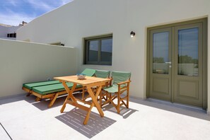 Eine Terrasse mit Tisch, Stühlen und einem grünen Sofa, sowie einer Tür.