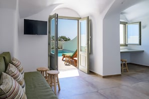 Ein modernes Wohnzimmer mit Fernseher, einer Couch, einem Essbereich mit Tisch und Stühlen sowie einer Glastür, die auf einen Balkon mit Pool führt.