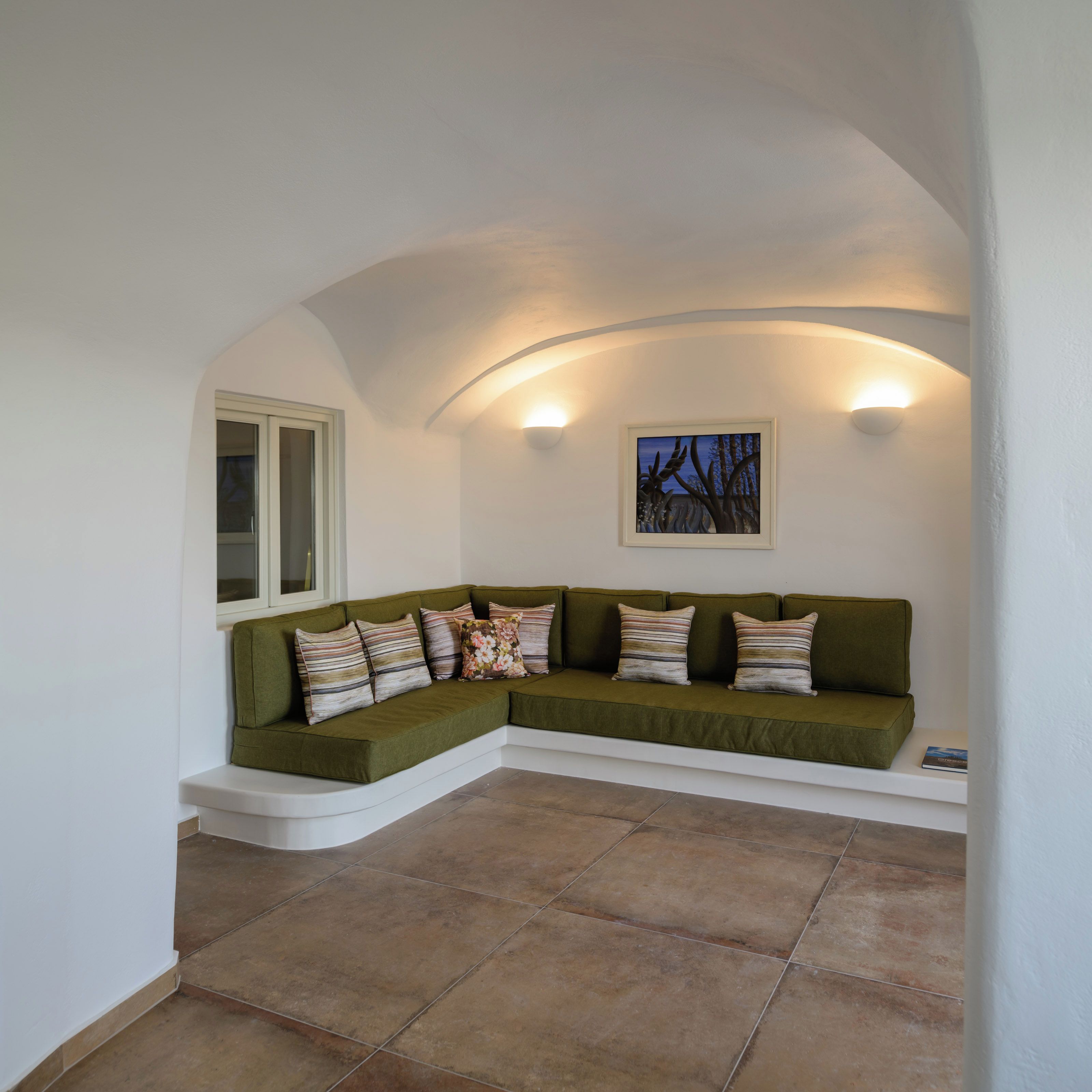 A corner seating area with a curved white bench, a wall-mounted painting, and a window.