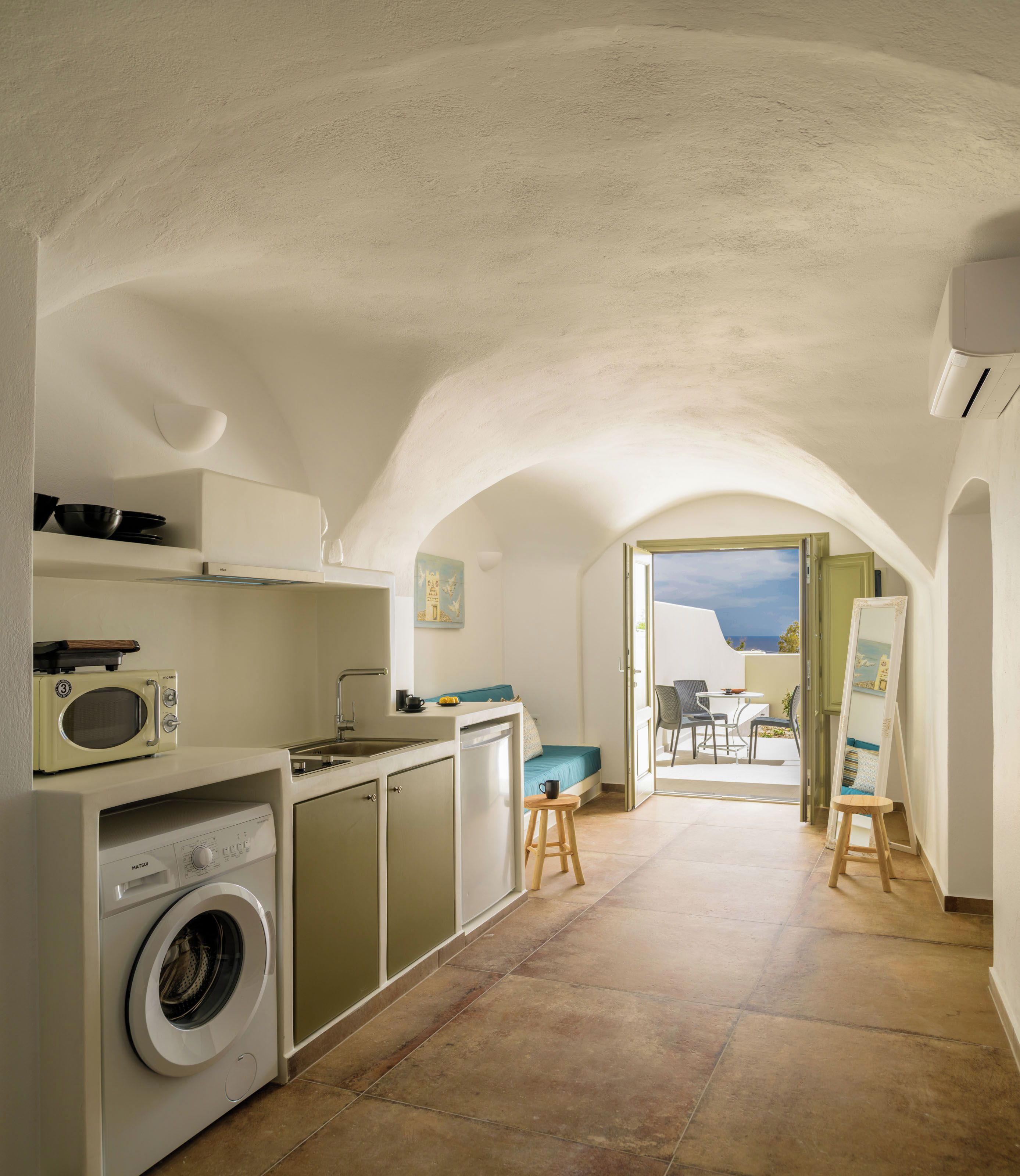 Cocina compacta con lavadora, microondas y lavabo. Cuenta con una zona de comedor con mesa y sillas, y vistas al exterior.