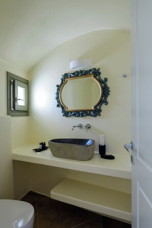 Ein Badezimmer mit einer freistehenden Badewanne, einem wandmontierten Spiegel mit aufwendiger Rahmenverzierung, einer Toilette und einem Fenster mit geschlossener Rolltreppe.