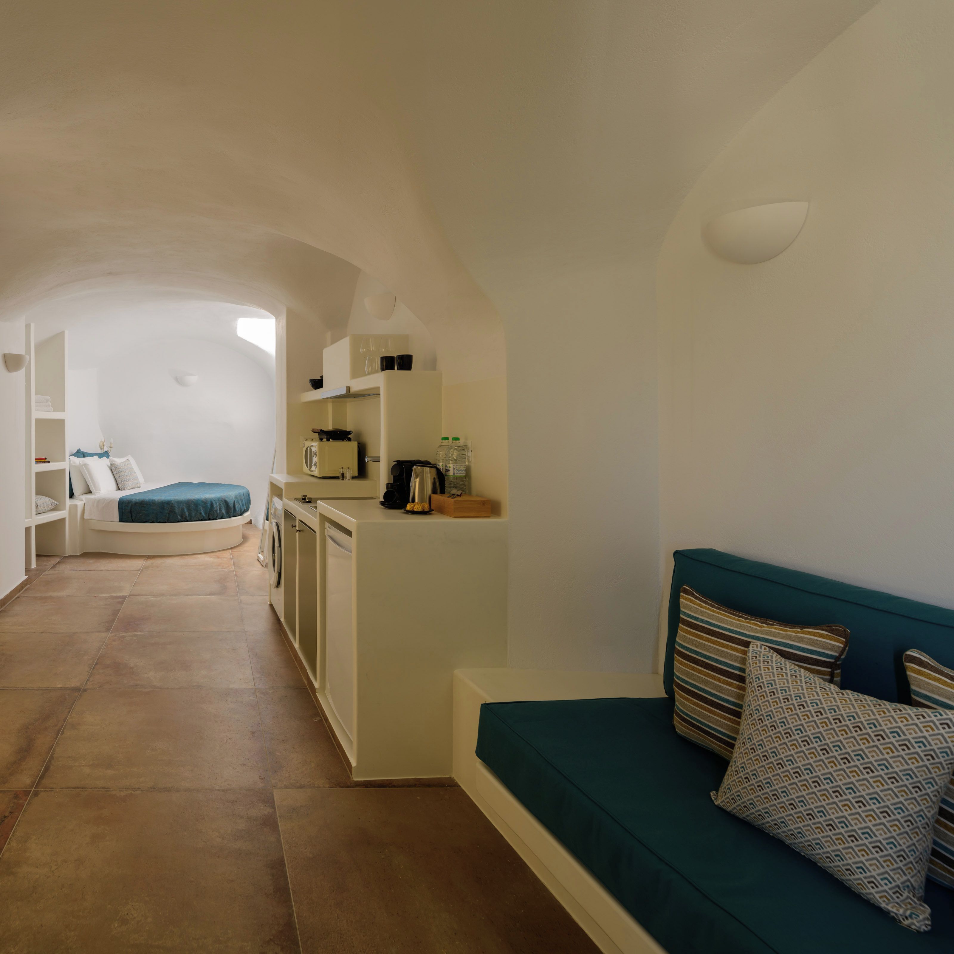 A compact living space with a kitchenette, a sofa, and a curved bed.