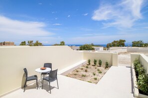 A rooftop terrace with a table and chairs, a small garden, and a view of the sea and distant buildings. - Little Garden Suite, Kaminia Holiday Homes (Exo Gonia)