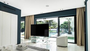 Een moderne hotelkamer met een bed, een glazen tv-meubel, een zithoek en uitzicht op een zwembad.