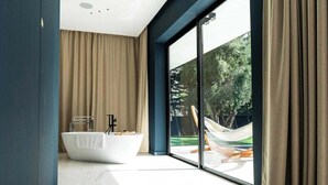 Een moderne badkamer met een vrijstaand bad, een groot raam en uitzicht op een hangmat buiten.