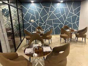 Uma sala de jantar moderna com design geométrico nas paredes, mesas redondas e cadeiras acolchoadas.