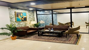 A lobby with a coffee table, sofas, chairs, a potted plant, and a painting on the wall. - Hotel Raaso Inn (Jaipur)