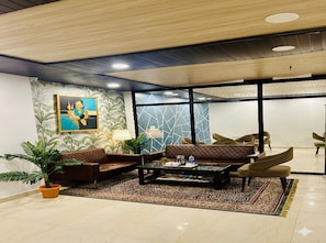 Eine Lobby mit Couchtisch, Sofas, Sesseln, einer Topfpflanze und einem Gemälde an der Wand.