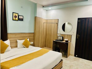 A hotel room with a bed, a desk, a mirror, a wardrobe, and two framed pictures on the wall. - Hotel Raaso Inn (Jaipur)