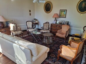 Ein Zimmer mit einem weißen Sofa, mehreren Stühlen, einem runden Tisch und einem gemusterten Teppich.