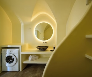 Casa de banho compacta com máquina de lavar roupa, lavatório com cuba, espelho com iluminação por baixo e toalheiro.