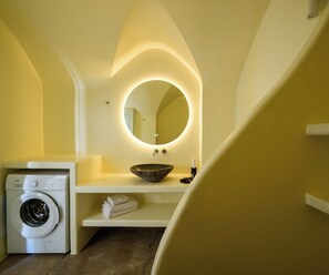 Ein kleines Badezimmer mit Waschmaschine, Waschbecken mit Schüsselbecken, Spiegel mit indirekter Beleuchtung und Handtuchhalter.