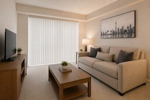 A modern living room with a sofa, coffee table, TV, and a cityscape painting. - Solara & Slate Hotel (Toronto)