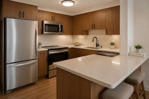 A modern kitchen with stainless steel appliances, wooden cabinets, a central island, and a built-in microwave. - Solara & Slate Hotel (Toronto)