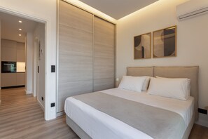 Ein modernes Schlafzimmer mit einem großen Bett, einem Schiebetürenschrank und einer durch eine offene Tür sichtbaren Küche.