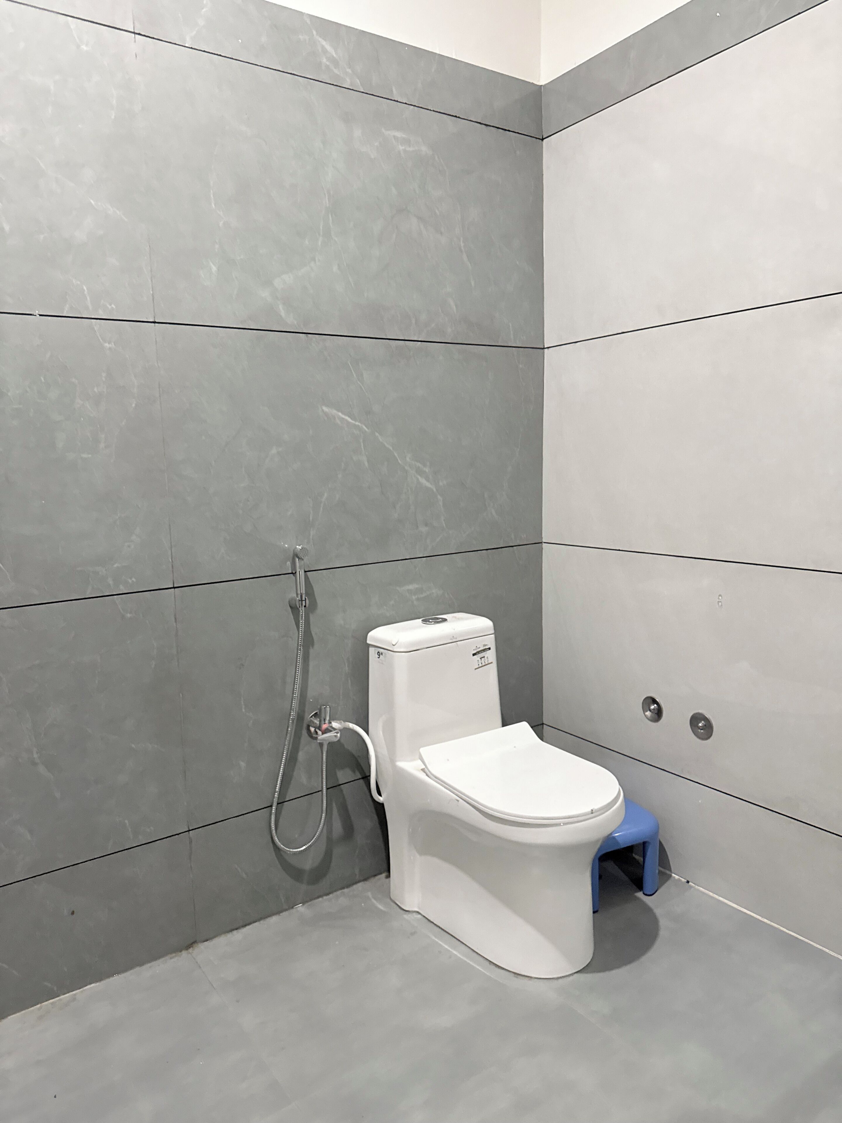 A modern bathroom with grey tiles, a white toilet, and a shower unit.