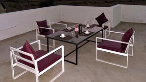 En tagterrasse med et glasbord, hvide stole med røde hynder og udsigt til fjerne bjerge.