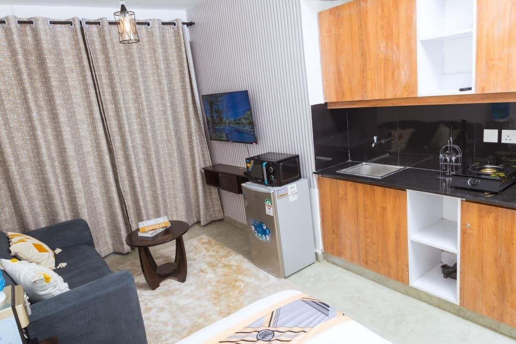 A compact living space with a kitchenette, a sofa, a small table, and a painting on the wall.