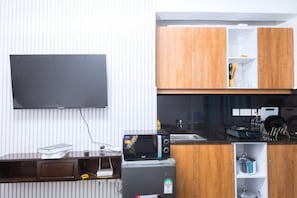 Eine kompakte Küche mit Mikrowelle, kleinem Kühlschrank, Holzschränken und einem flachbildfernseher an der Wand.