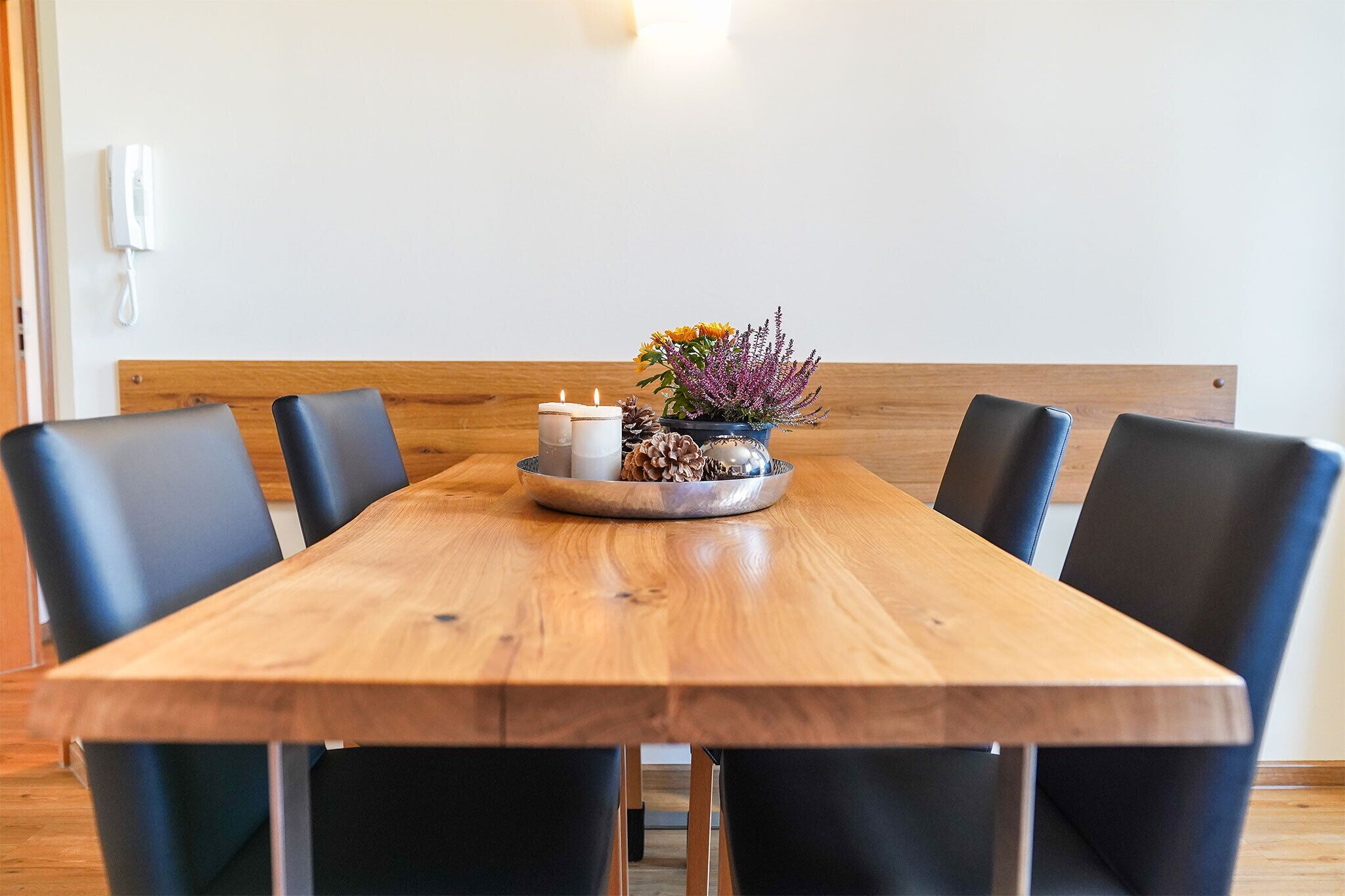 Ein Holztisch mit sechs schwarzen Stühlen, eine kleine Blumenkomposition und zwei Kerzen.
