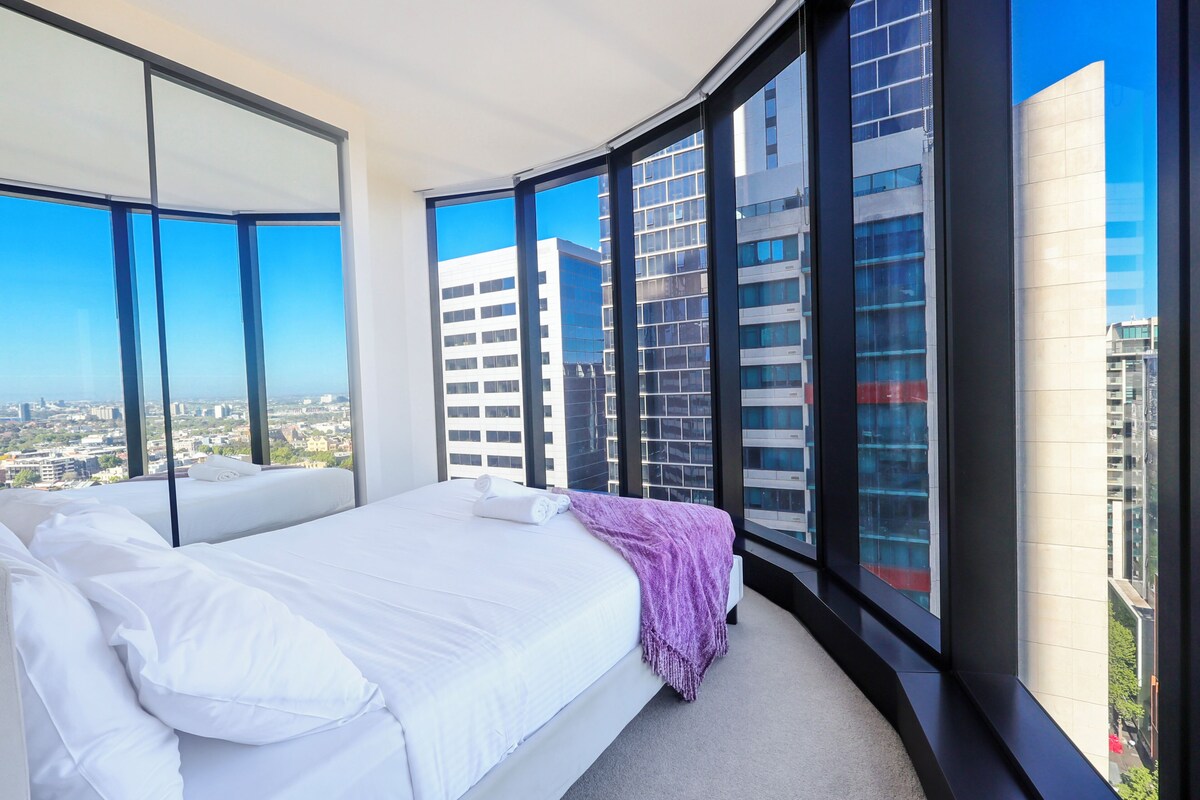 Ein modernes Schlafzimmer mit einem großen Bett, Blick auf die Stadt und einem Eckfenster.