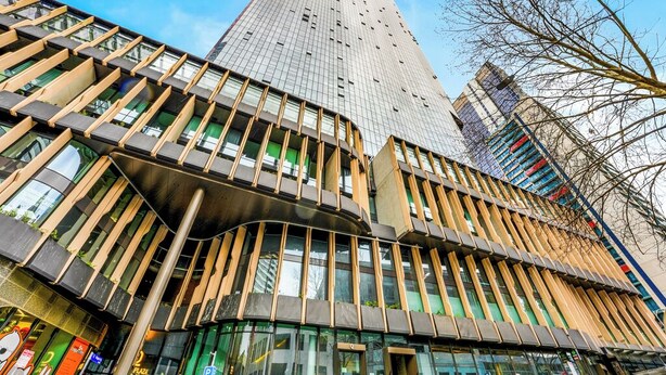 A modern building with a curved facade, large windows, and a prominent tower in the background. - SKY HIGH Apartment (Melbourne)