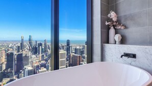 A modern bathroom with a large bathtub, a vase with flowers, and a city view. - SKY HIGH Apartment (Melbourne)