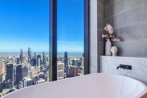 Ein modernes Badezimmer mit einer großen Badewanne, einem Blumenstrauß und Blick auf die Stadt.