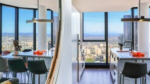 A modern kitchen with large windows, a dining area, and a view of the cityscape. - SKY HIGH Apartment (Melbourne)