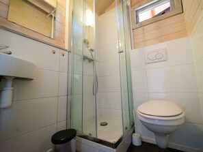 Een badkamer met een douchecabine van glas, een toilet, een wastafel en een klein raam boven het toilet.
