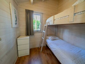 Een kleine kamer met een enkel bed, houten wanden, een raam met gordijnen, een witte kapstok en een ladder.